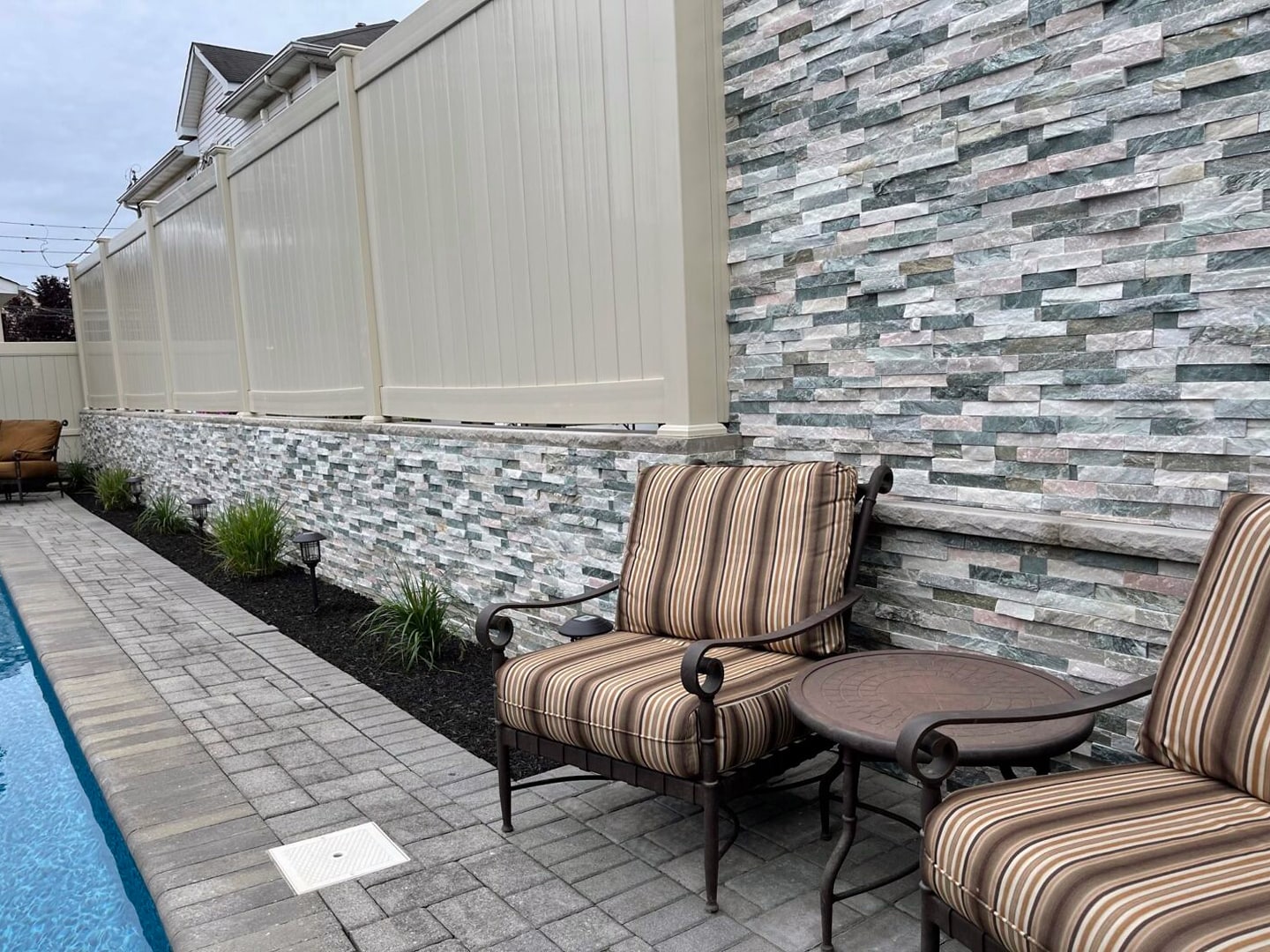 Two cushioned chairs by pool, stacked stone wall and vinyl fence
